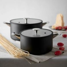 two black pots sitting on top of a table next to some red berries and pasta