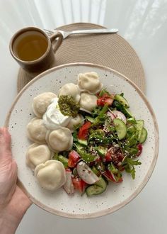 a white plate topped with veggies and dumplings next to a cup of tea