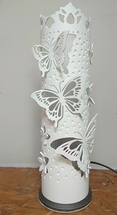 a white lamp with butterflies on it sitting on top of a wooden floor next to a wall