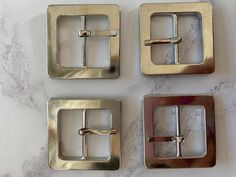 three square metal buckles on a marble surface