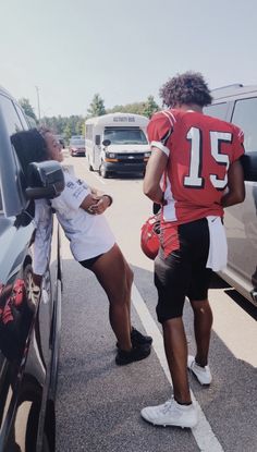 two people in football uniforms standing next to cars