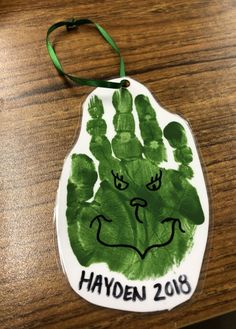 a handprinted ornament on a wooden table with green ribbon hanging from it