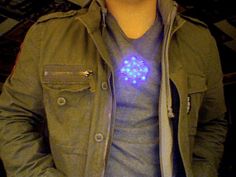 a man wearing a green jacket has a blue light on his shirt and is holding a cell phone