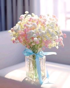 a vase filled with white and pink flowers on top of a window sill next to a blue ribbon