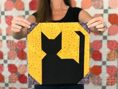 a woman holding up a piece of art made out of quilts and fabric with the shape of a cat's head on it