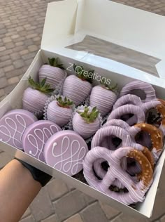 a person holding a box full of purple chocolate covered strawberries and pretzels