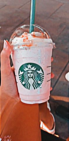 a woman holding up a starbucks drink with whipped cream on top and a green straw in her hand