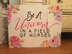 a wooden sign that says, be a unicorn in a field of horses on it