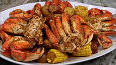 crab legs, corn and potatoes on a white plate