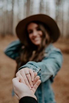 a woman holding the hand of a man who is wearing a hat and jeans jacket