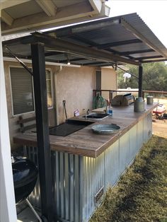 an outdoor kitchen made out of metal and wood with a grill attached to the roof