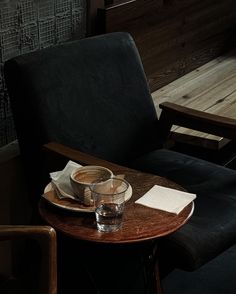 a wooden table topped with a cup of coffee next to a black chair and window