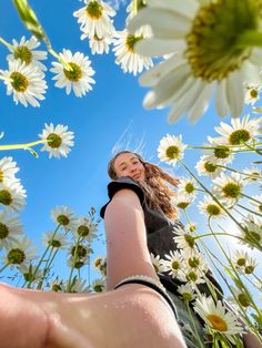 a woman is holding out her hand in front of some daisies and blue sky