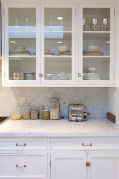 a kitchen with white cabinets and marble counter tops in the center, filled with dishes