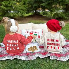 two young children sitting on a blanket eating cookies and muffins while wearing matching christmas sweaters