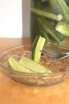 a jar filled with cucumber slices on top of a wooden table next to a spoon