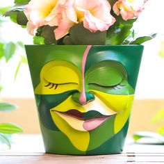 a green planter with a face painted on it and pink flowers in the background