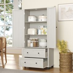 a white cabinet with drawers and baskets on the bottom shelf next to a table in front of a window