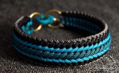 a blue and black braided bracelet sitting on top of a gray cloth covered floor