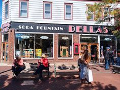 people are sitting on benches in front of a store with soda fountain delias