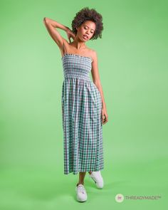 a woman in a green and white checkered dress poses for the camera with her arms behind her head