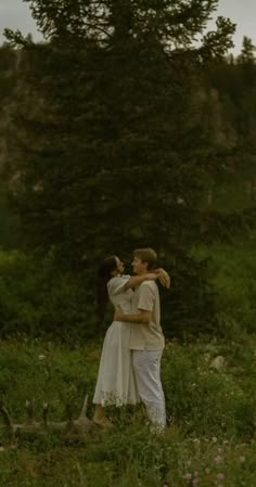 a man and woman standing in the grass with trees in the backgrouund