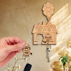 a hand holding a wooden keychain with a house on it and balloons in the air