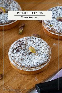 three pastries on a wooden cutting board covered in powdered sugar and pistachio