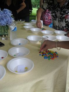 people are standing around a table with white bowls on it and colorful beads in the middle