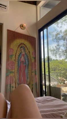 a woman laying on top of a bed in front of a window next to a painting