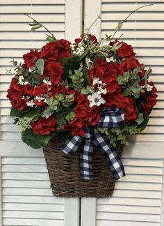 red and white flowers in a basket hanging on the side of a door with a bow