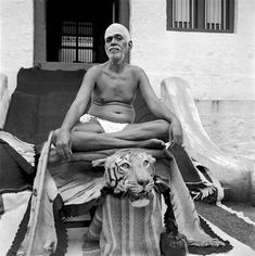 an old man sitting in front of a building with a tiger statue next to him