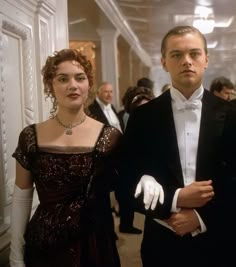 a man in a tuxedo standing next to a woman wearing a dress and gloves