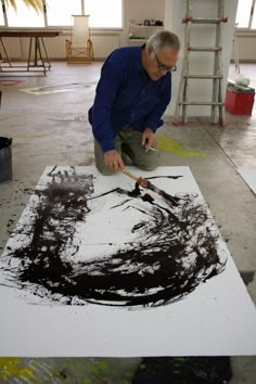 a man sitting on the ground working on an art piece with black paint and scissors