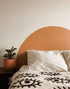 a bed with an orange headboard and white sheets in front of a potted plant