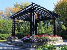 an outdoor gazebo with flowers in the foreground and trees in the back ground