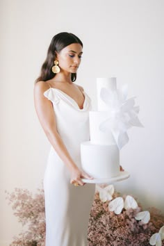 a woman in a white dress holding a cake with a large bow on it's top