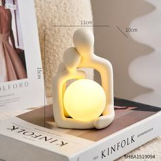 a white light sitting on top of a book next to a lamp that is shaped like a kissing couple