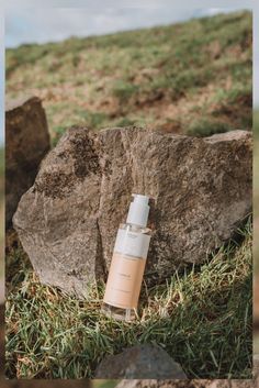 an empty bottle sitting in the grass next to some rocks