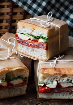 several sandwiches wrapped in brown paper sitting on top of each other, with one sandwich cut in half