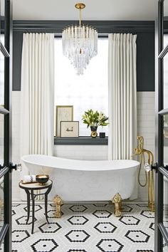 a white bath tub sitting under a chandelier in a bathroom next to a window