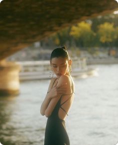 a woman in a black dress standing by the water