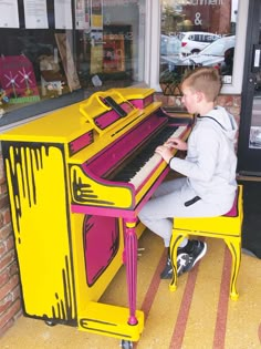 a young boy sitting at a brightly colored piano in front of a storefront window