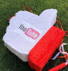 a fake youtube heart sitting on top of green grass next to a red and white box