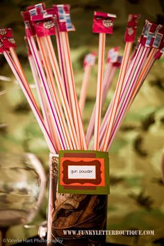 several red and white striped straws in a glass vase with wine glasses behind it