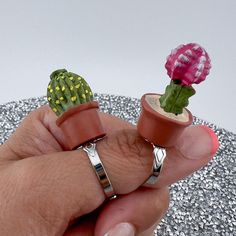 a person holding two small rings in their hand with a cactus plant on the other side