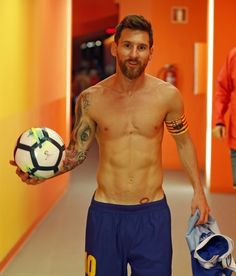 a shirtless man holding a soccer ball in his right hand while walking down a hallway