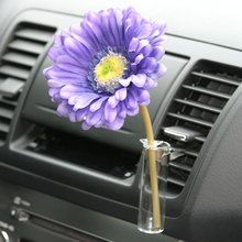 a purple flower in a clear vase on the dashboard of a car with air vent