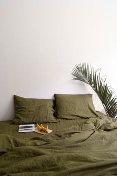 a bed with green sheets and pillows next to a potted palm plant on the side