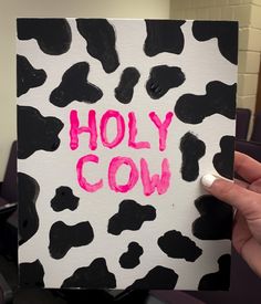 a hand holding up a piece of paper with the words holly cow painted on it